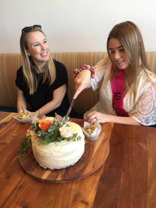 two girls sitting down in front of a cake